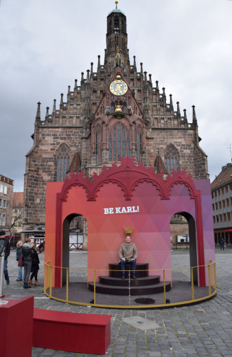 Mann auf Krönungsstuhl vor Kirche. Schriftzug "Be Karl!"
