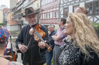 ein Mann mit einer Geige, daneben eine Frau mit langen offenen blonden Haaren, die singt