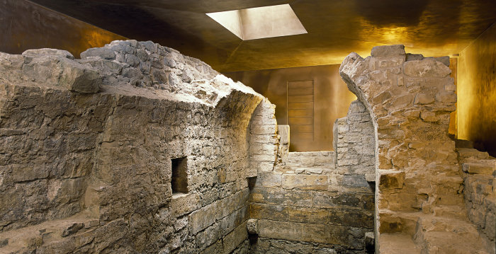 Foto: Mikwe Erfurt © Peter Seidel Mauerreste der mittelalterlichen, jüdischen Mikwe. Reste eines kleinen Raumes mit Tonnengewölbe, umgeben von Ausschnitten des bronzefarbenen Schutzbaus.