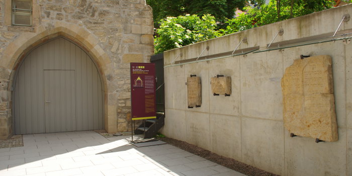 Rechts drei mittelalterliche Grabsteine montiert an einer Wand, im Hintergrund der Eingang zum Museum.