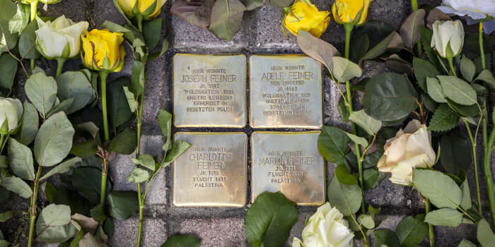 im Boden sind vier Messingplatten mit Inschrift verlegt, rundherum liegen weiße und gelbe Rosen