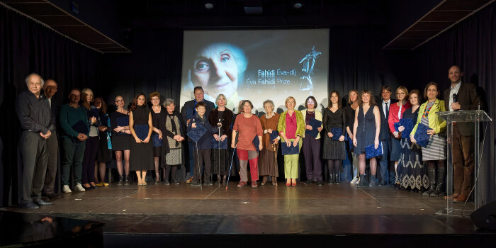 eine große Anzahl von Personen steht auf einer Bühne vor einer Leinwand mit dem Porträt einer Frau