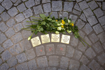neben vier im Boden eingelassenen Messingsteinen liegen gelbe und weiße Rosen