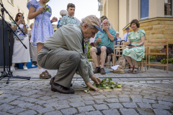 ein älterer Mann legt eine Rose an vier im Boden eingelassenen Messingsteinen nieder und berührt sie mit der Hand