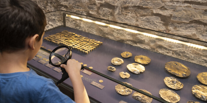 ein Kind schaut mit der Laupe auf Münzen in einer Vitrine