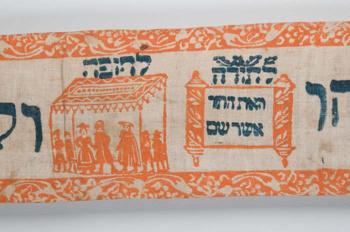 ein Ausschnitt aus einem Torawimpel mit orangefarbenen Bildern und schwarzer Schrift