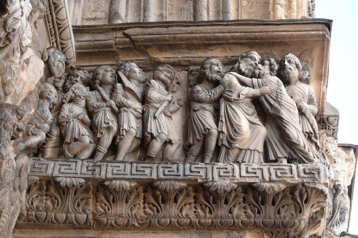 Die Aufnahme zeigt ein Relief an einer Kirche. Judas  küsst Jesus auf die Wange, andere Jünger stehen daneben. 