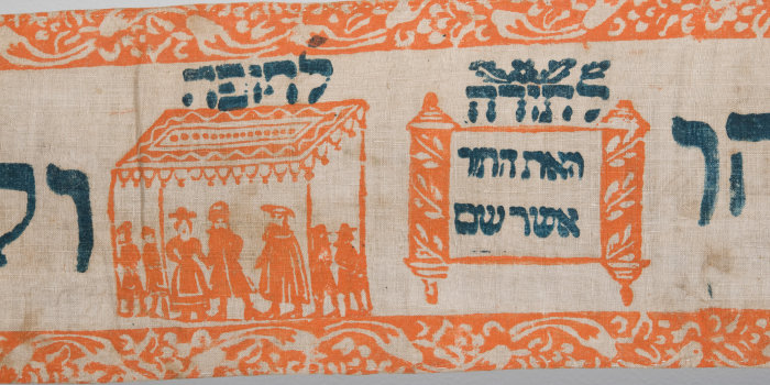 ein Ausschnitt aus einem Thorawimpel mit orangefarbenen Bildern und schwarzer Schrift