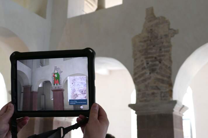 Raum in einer Abteikirche mit einem Tablet mit Augmented Reality-Darstellung der Stuckfiguren