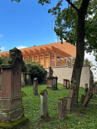 Gebäude mit hellen Holzbalken in der Bauphase mit Friedhof im Vordergrund