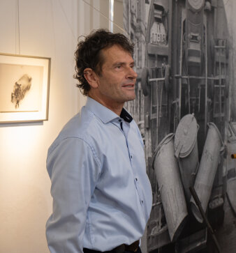 Mann mittleren Alters im hellblauem Hemd vor einem Bild stehend