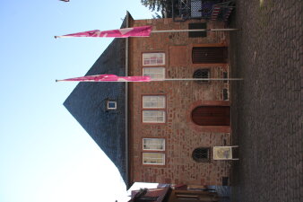 Außenansicht eines Backsteingebäudes mit zwei Fahnen im Vordergrund