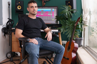 Junger Mann auf einem Stuhl sitzend in einem Musikstudio, umringt von Instrumenten, einem Mikrofon und PC