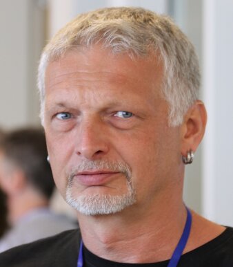 Mann mit hellgrauen Haaren, kurzem Bart und Ohrringen