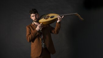 Mann mittleren Alters in einem braunen Sakko mit dem Intsrument Lavta