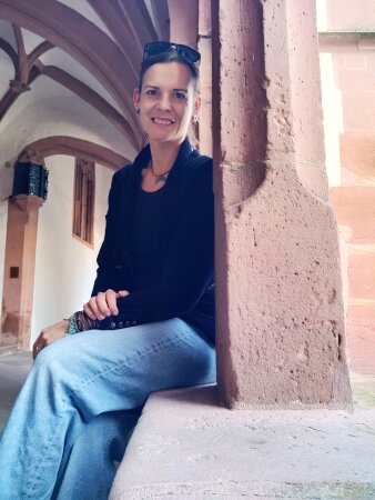 Frau mittleren Alters mit Sonnenbrille auf einem Stein sitzend