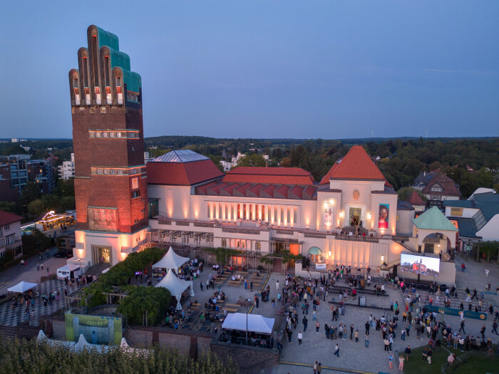 Besonders kunstvolles Gebäude mit einem hohen Turm umrahmt von einem Platz mit Menschen