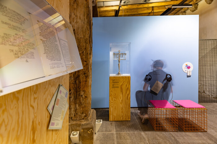 Eine männliche Person an einer Hörstation in einer Ausstellung mit Exponaten und Hockern mit pinken Kissen