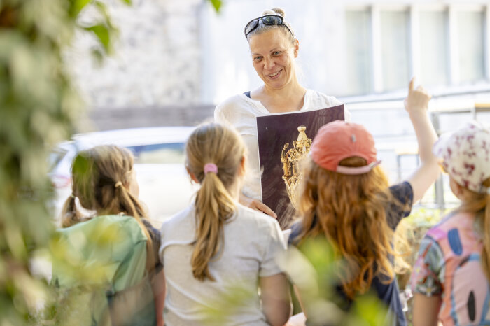 Eine Frau mit Sonnebrille zeigt vier Kindern ein Bildmotiv des Erfurter Schatzes