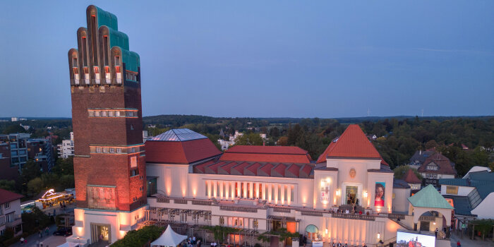 Besonders kunstvolles Gebäude mit einem hohen Turm umrahmt von einem Platz mit Menschen