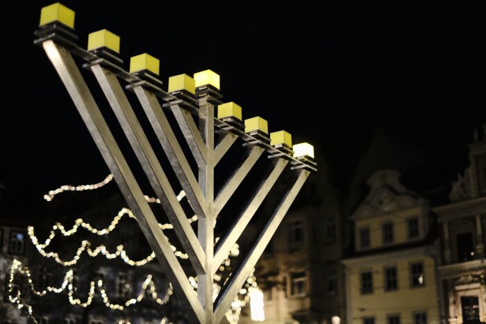 Achtarmiger Chanukka-Leuchter auf dem Erfurter Fischmarkt mit brennenden ersten Licht vor weihnachtlicher Kulisse