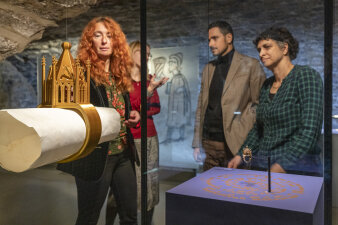 vier Menschen stehen an einer Ausstellungsvitrine, im Vordergrund ein Ausstellungsobjekt