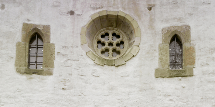 Fassadenausschnitt. Ein großes, rundes Rosettenfenster wird von zwei kleineren Lanzetfenstern flankiert