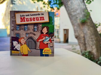 Ein buntes Pixi-Buch mit dem Gebäude der Alten Synagoge Erfurt im Hintergrund