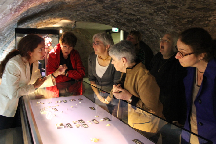 A group of people is standing around a showcase containig jewellery from the Erfurt Treasure, discussing animatedly.
