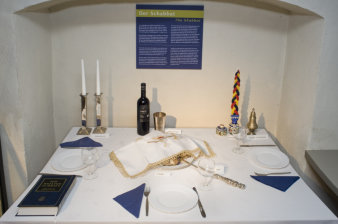 Festively laid table with three plates, cutlery, wine glasses, a bottle of wine and candles in the background