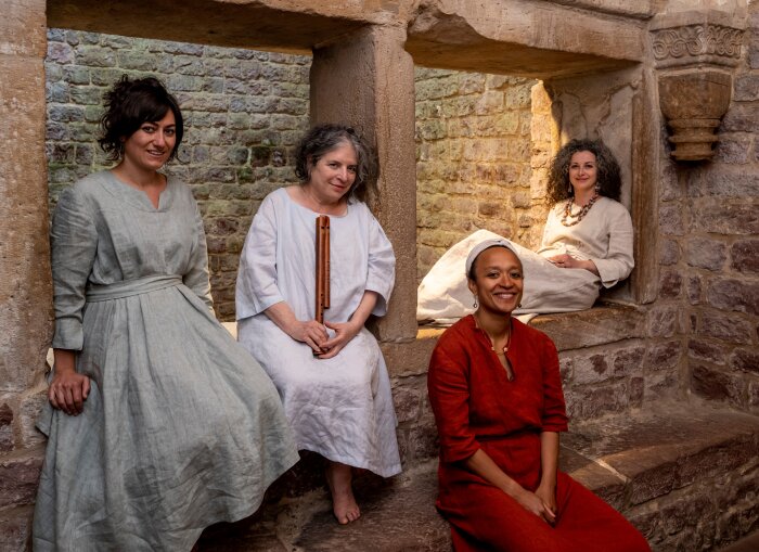 Frauen in mittellaterlichen Gewändern auf einer Mauer sitzend