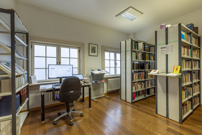 Ein Raum mit Schreibtisch samt PC und Büchern befüllten Regalen