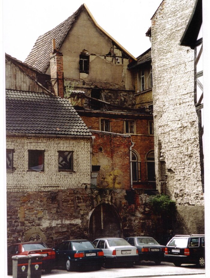 Ostgiebel vor dem Umbau Blick auf eine Runie, davor ein Parkplatz mit beschädigter Mauer.