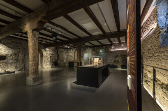 Blick in einen Ausstellungsraum mit Holzbalken und steinernen Wänden