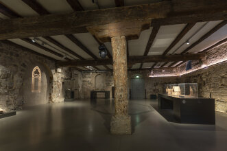 Blick in einen Ausstellungsraum mit Holzbalken und steinernen Wänden
