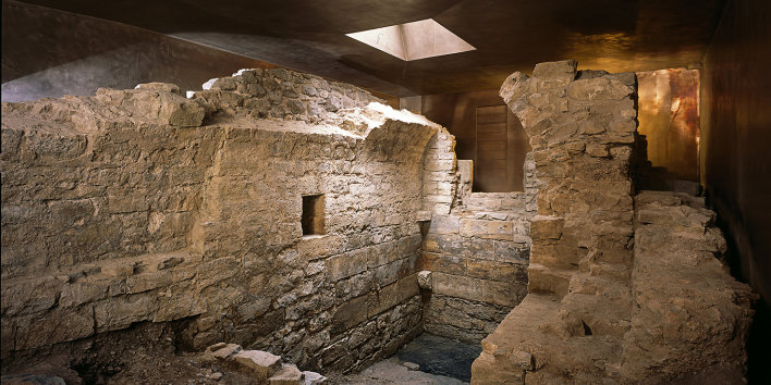 Ruined walls of the mikveh, encased by bronze-coloured protective building