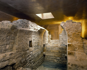 Ruined walls of the mikveh, encased by bronze-coloured protective building