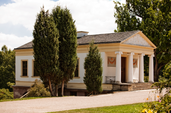 Foto: Weimar, Römisches Haus im Park an der Ilm © Klassik Stiftung Weimar, Jens Hauspurg Ein Haus nach Art eines griechischen Tempels mit Säulenvorbau, weis-gelb gestrichen, steht im Sonnenlicht in einer Parklandschaft.