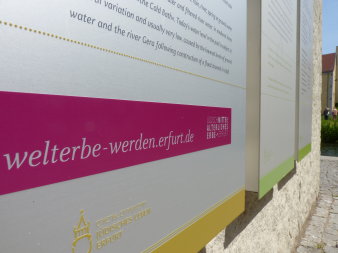 Drei Infotafeln an der mittelalterlichen Mikwe mit purpurfarbenen Band und Hinweis auf die Erfurter Unesco-Bewerbung