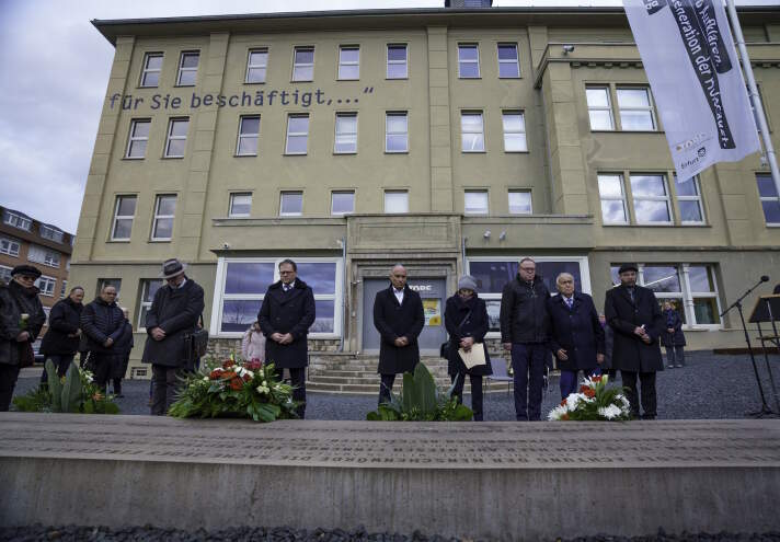 Mehrere Personen vor einem Gebäude die Blumen niederlegen