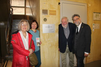 vier Personen stehen an einer Wand, an dem eine silberfarbene Plakette mit Schriftzug "Bethe-Stiftung" hängt